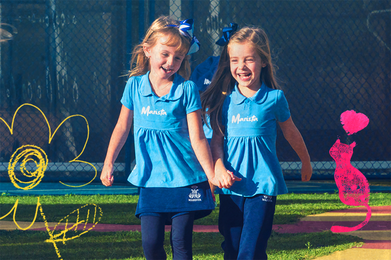 ensinar empatia: duas meninas de mão dadas sorrindo, com o uniforme dos Colégios Maristas.