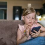 Menina loira fazendo uso excessivo do celular.