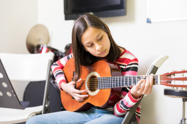 A imagem mostra uma garotinha tocando violão na sua atividade extracurricular.