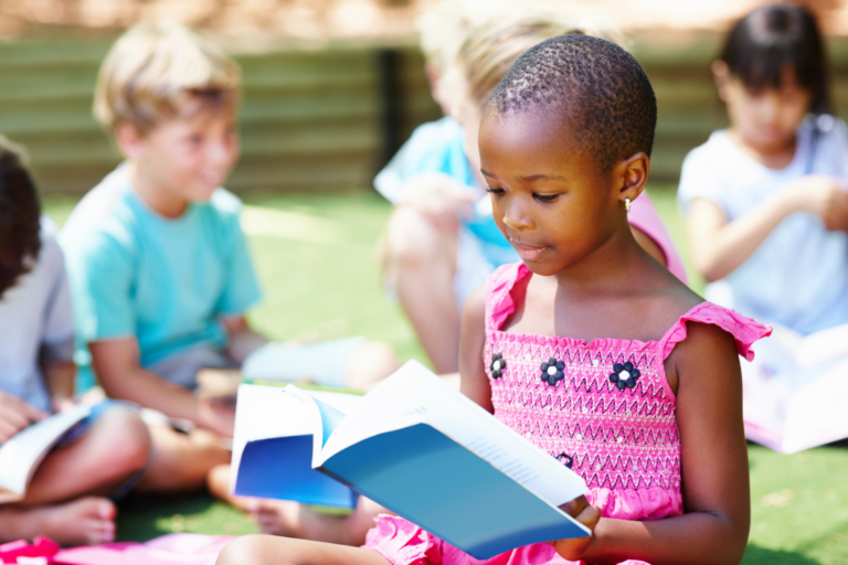 A imagem mostra uma criança com vestido rosa lendo um livro de capa azul.