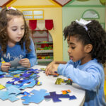 Duas crianças brincando de montar quebra cabeça na escola, representando práticas pedagógicas para a diversidade cultural na educação infantil.
