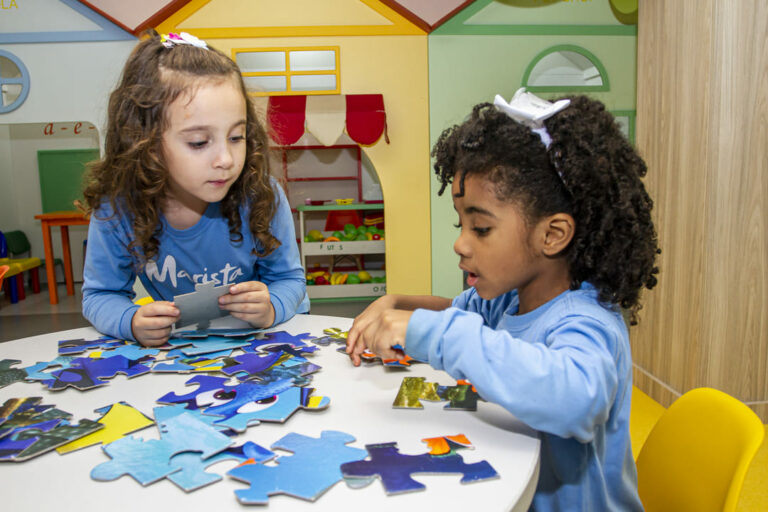 Duas crianças brincando de montar quebra cabeça na escola, representando práticas pedagógicas para a diversidade cultural na educação infantil.