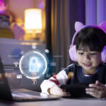 Criança com fone de ouvido utilizando o computador e celular com ilustração de cadeado à frente da tela, representando a segurança na internet.