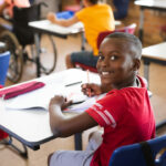 Menino sentado em carteira escolar, representando o aprendizado da história afro-brasileira.