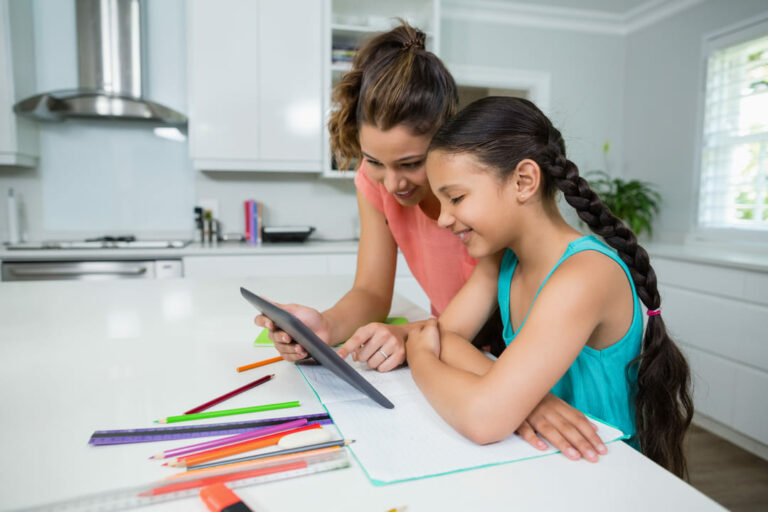 Mãe ajudando filha a fazer pesquisa escolar em casa.